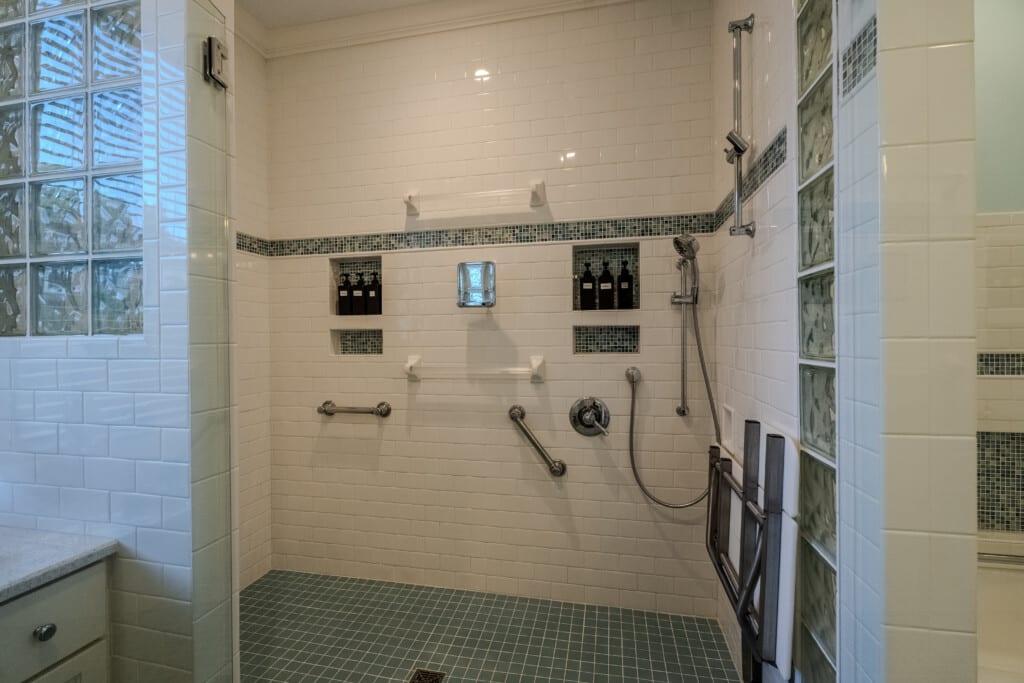 A wall-mounted shower seat, hand-held shower, and grab bars help guests feel considered, supported, comfortable, and prepared.