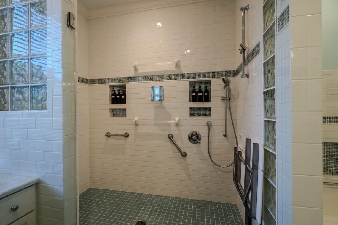 A wall-mounted shower seat, hand-held shower, and grab bars help guests feel considered, supported, comfortable, and prepared.